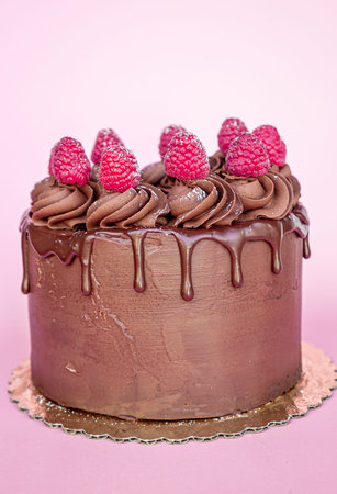 Valentine's day chocolate cake decorated with chocolate icing and red fruits on top sprinkled with...