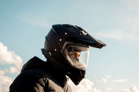 Motorcyclist wearing a black dual-purpose motorcycle helmet with a black jacket looking skyward.の写真素材