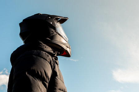 Motorcyclist wearing a black dual-purpose motorcycle helmet with a black jacket looking skyward.