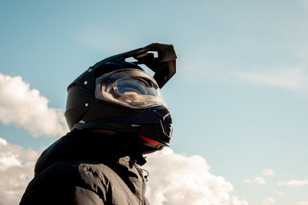 Motorcyclist wearing a black dual-purpose motorcycle helmet with a black jacket looking skyward.
