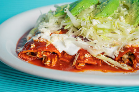 traditional Mexican red chicken enchiladas, with chopped lettuce, sour cream, cheese and avocado on...