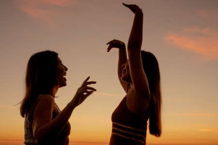 Latin girls dancing on the beach with a sunset in the backgroundの写真素材
