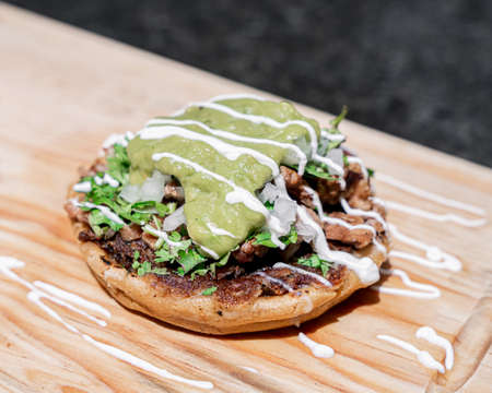 Appetizing Mexican sope with meat, onion, cilantro, cheese, cream and guacamole, served on a board.の写真素材