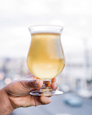 Exquisite light beer with foam, served in a glass and held in one hand.の写真素材