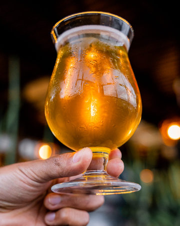 Delicious amber beer with foam, held by a hand, and with a background of lights.