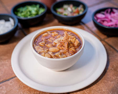 Exquisite Mexican style birria broth with beans from the pot, served in a deep white dish, with sauces and condiments on the bottom.の写真素材
