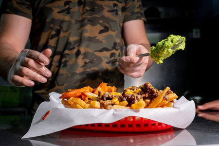 person preparing nacho cheese fries with yellow cheese, carne asada and a lot of guacamole