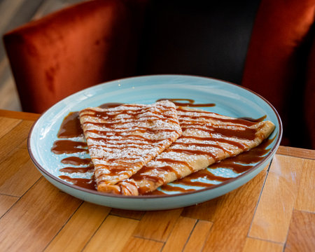 Delicious Mexican style cajeta crepe with icing sugar on top on a blue plate.の写真素材