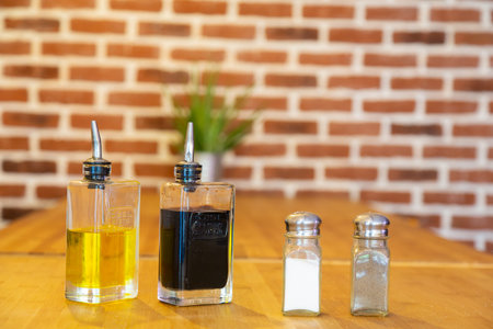Pepper mill and salt shaker, with bottles of oil and vinegar, on a bamboo table with a brick...