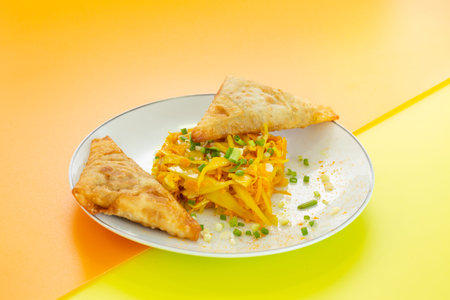 Green papaya and carrot salad with samoussas in a plate on a yellow and orange background