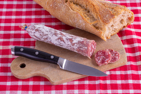 Sausage on a wooden cutting board on a red tile tableclothの写真素材