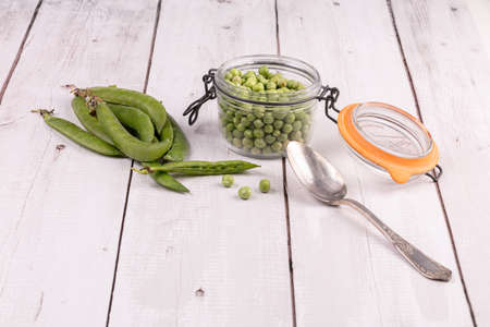 Shelled peas in a glass jar with the pods on the side on a white wooden tableの写真素材