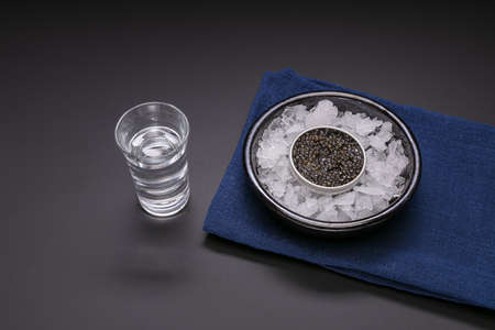 Caviar in a metal box with a glass of vodka on black backgroundの写真素材