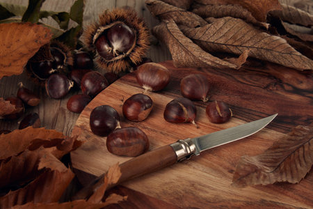 Chestnuts and leaves with knife on a wooden table