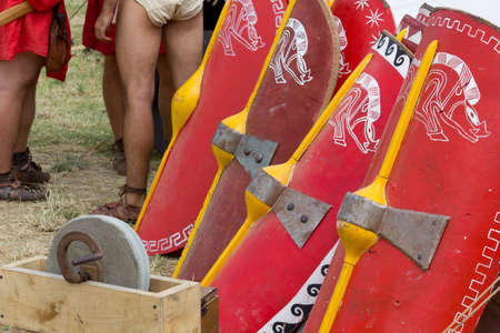 A row of decorated legionary shields, a grinder and a few soldiers in an ancient roman encampmentの写真素材