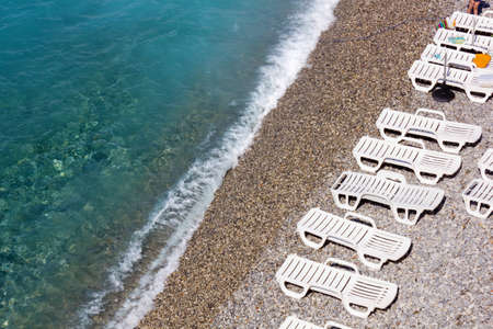 Above view of the shoreline on a pebble beach with some beach loungersの写真素材