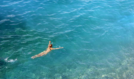 Above view of a young woman swimming in a turquoise blue seaの写真素材