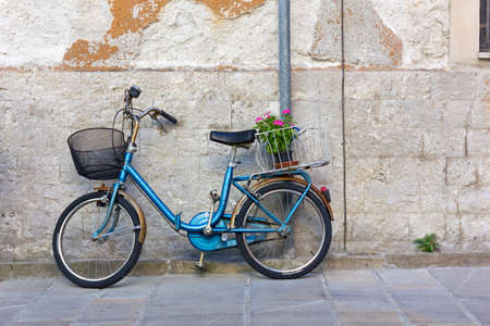 Blue vintage bicycle against an exterior wall with a flowerpot in its rear basketの写真素材