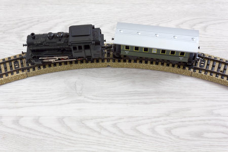 Model electric train formed by a vintage steam locomotive and a green passenger car on the rails...