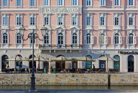TRIESTE, Italy - May 17, 2017: Street life in Via Rossini, along Canal Grande, with outdoor tables, people strolling, a classic streetlamp in the foreground and a historic palace in the backgroundのeditorial素材