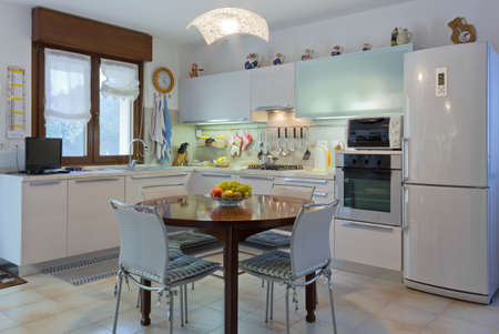 Italian modern white home kitchen interior with round wooden table and tiled floorの写真素材
