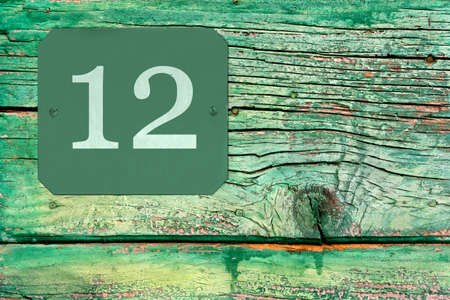 Street number 12 sign on the wooden surface of an old ruined green doorの写真素材