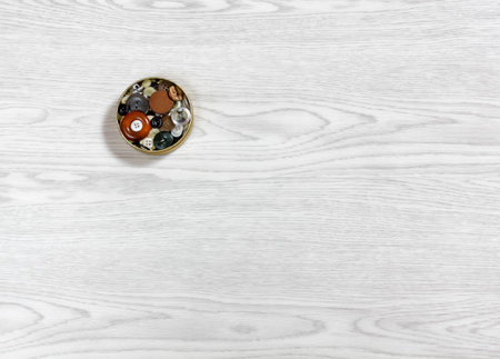 Small metal box full of buttons of various shapes and sizes on a white wooden background