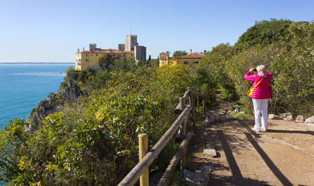 DUINO AURISINA, Italy - October 23, 2017: A woman photographs the castle of Duino, on the cliffs of the rocky coastline near Trieste, Italyのeditorial素材