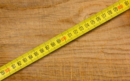 Segment of a yellow metal measuring tape placed diagonally on an old wooden table