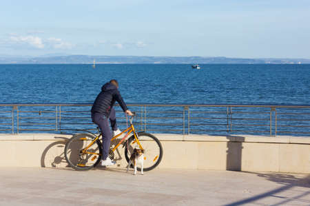 GRADO, Italy - April 13, 2018: A man on his bicycle on the seafront watching the sea with his dog on the leashのeditorial素材