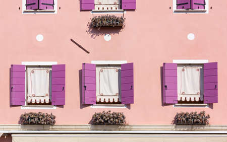 Detail of a decorated pink colored house's exterior with purple window shuttersの写真素材