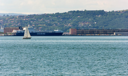 TRIESTE, Italy - June 5, 2013: A sailboat in front of a docking area of the port, with a container...