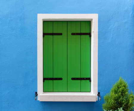 Close-up on the colorful exterior of a traditional house in the venetian style with a closed window with green shuttersの写真素材