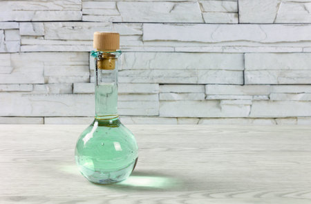 Small bottle on a wooden table, closed by a cork and full of a turquoise green colored drink