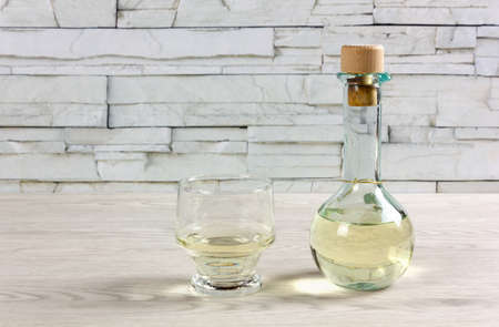 A small bottle on a wooden table, closed by a cork, full of white wine and next to a glassの写真素材