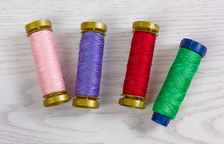 Four thread spools of different colours on a white wooden backgroundの写真素材