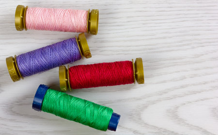 Four thread spools of different colours on a white wooden background