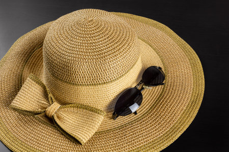 Straw hat with a big bow on a dark wooden background, with a pair of  sunglasses