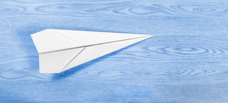 White paper airplane over a wooden blue background resembling a blue sky