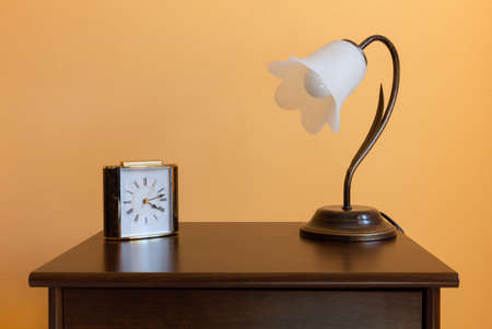 A classic flower-shaped lamp and an alarm clock on a wooden nighstandの写真素材