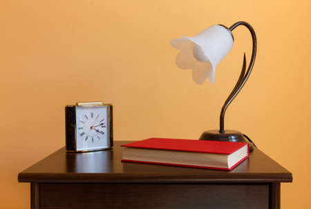 A classic flower-shaped lamp, an alarm clock and a book on a wooden nighstandの写真素材
