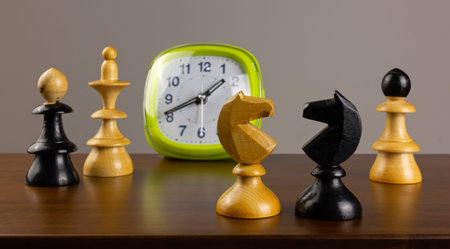 Two knights facing each other on a wooden table, with an alarm clock and other chess pieces in the...