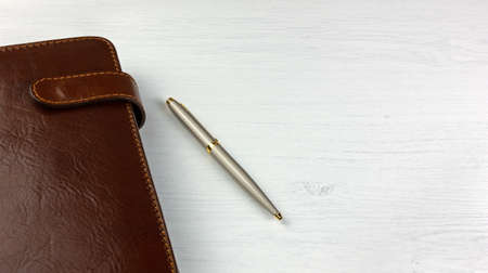 Elegant pen and daily planner with a leather cover on a white wooden deskの写真素材