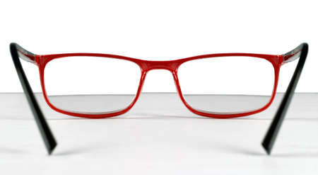 First person view of a pair of red eyeglasses lying on a table over a white backgroundの写真素材