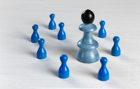 A big pawn with a black head surrounded by smaller pawns on a white wooden table