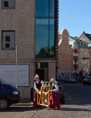 RIGA, Latvia - July 17, 2013: Two women wearing a folk costume are carrying a traditional wooden artifact on a street in downtown Rigaのeditorial素材