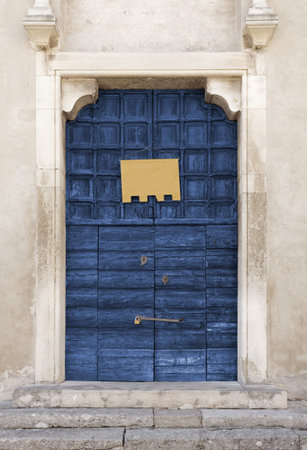Old wooden blue-colored portal of an ancient church, with an empty yellow banner hung on it