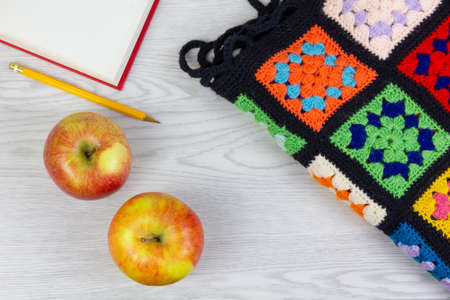 Above view of two yellow and red apples, a multicolor plaid blanket, an open book and a pencil on a white wooden tableの写真素材