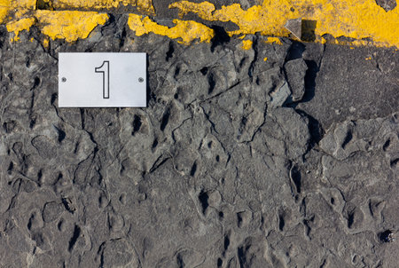 Asphalt background with a yellow strip on top and a white screwed-in tile with number one printed on...
