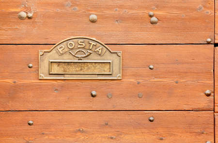 Metal maibox opening on the surface of a wooden exterior front door with the italian word for mailの写真素材